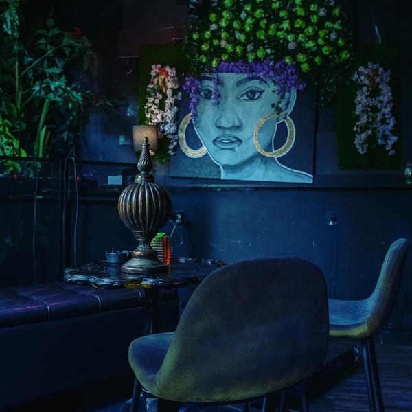 Dark, intimate corner of Lydia on H with a large mural of an African woman and lush greenery.