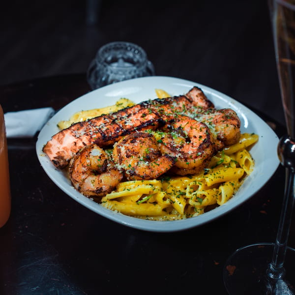 Grilled salmon and shrimp over penne pasta with a creamy sauce, garnished with parsley and cheese.