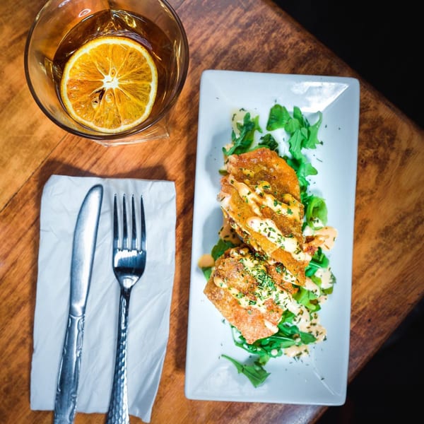 African-inspired fried plantains with sauce and greens, next to a drink with an orange slice.
