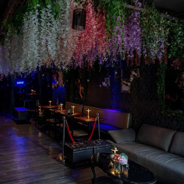 Dark, moody restaurant interior with hanging floral decor, booth seating, and glowing table lamps.