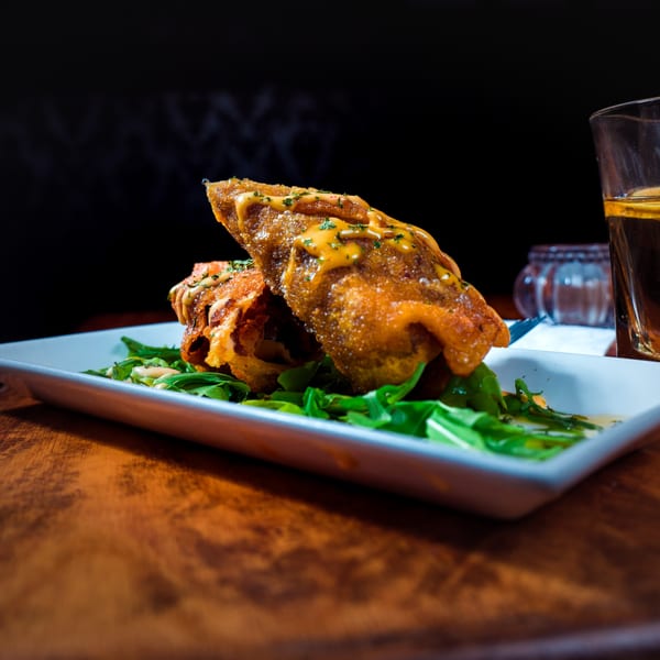 Two golden-fried African pastries drizzled with sauce and herbs, served on a bed of greens.
