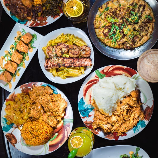 Overhead view of various African dishes including chicken, rice, pasta, and pizza on a dark table.