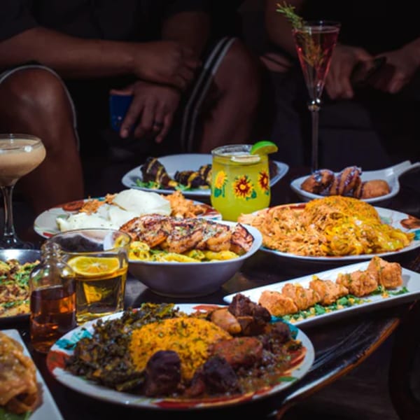 A table laden with various African dishes and drinks, with people in the background.