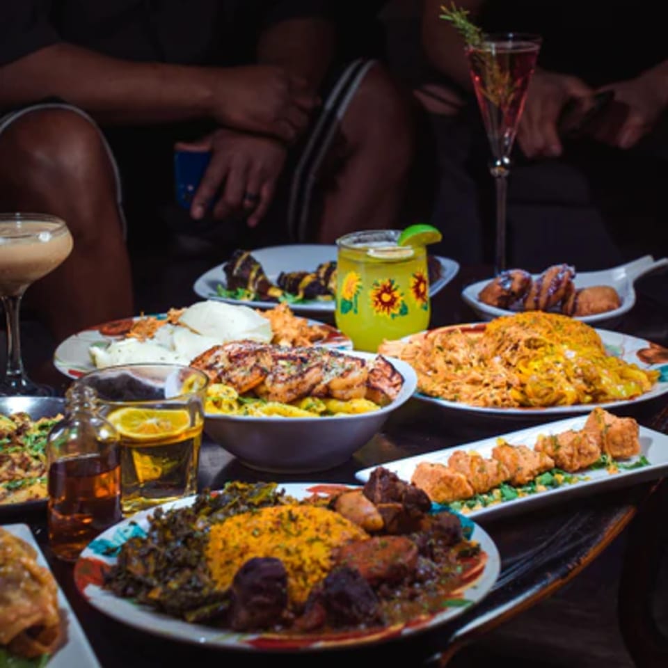 A table laden with various African dishes and drinks, with people in the background.